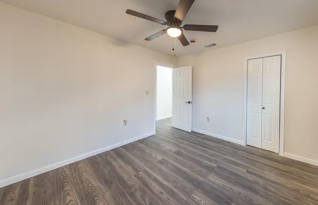 an empty room with wooden floor ceiling fan and window