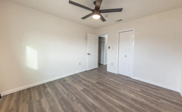 an empty room with wooden floor ceiling fan and windows