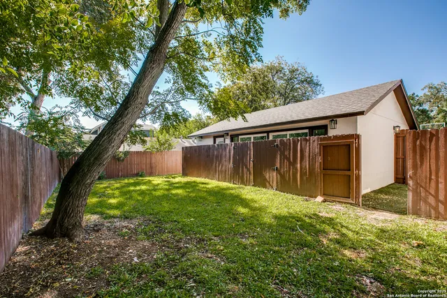 a view of backyard with large tree and wooden fence