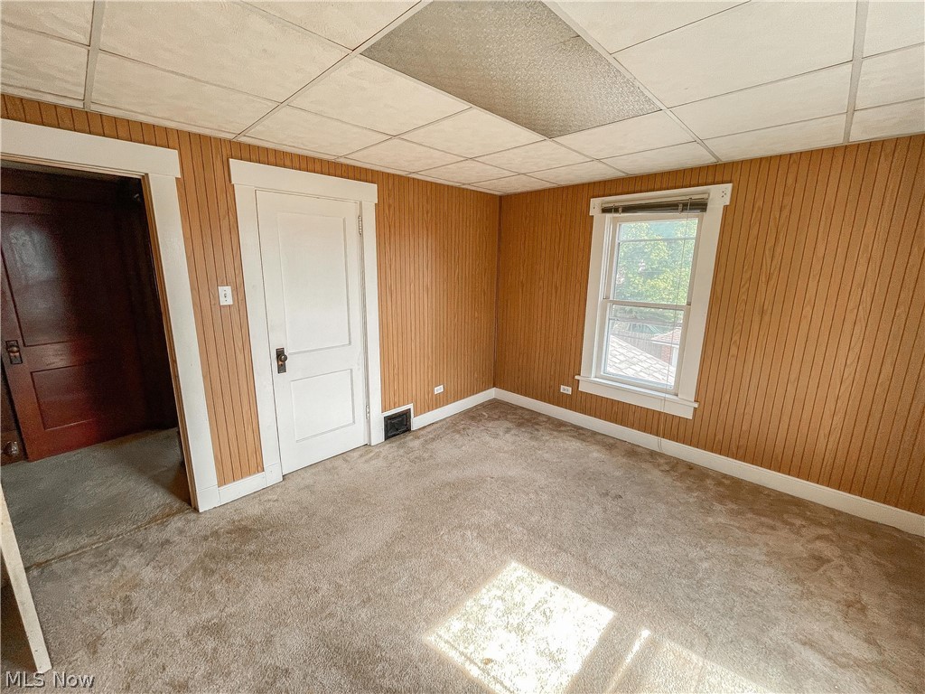 2811 9th Street Northwest Canton, OH 44708 - Photo 15 of 20 Empty room featuring carpet, wooden walls, and a drop ceiling