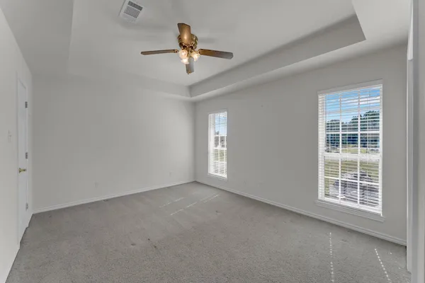 an empty room with chandelier fan and windows