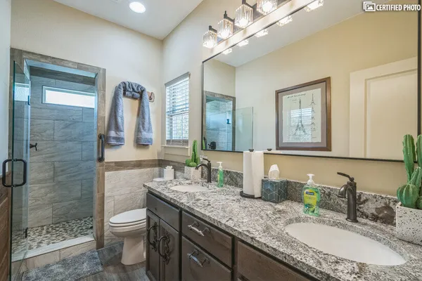 a bathroom with a granite countertop double vanity sink a toilet and a mirror