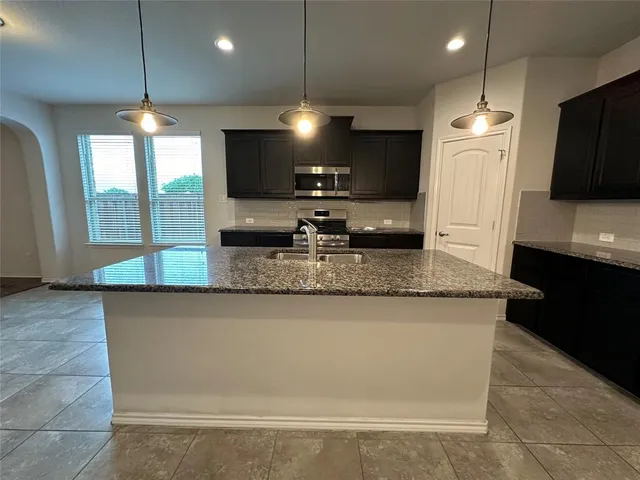 a kitchen with kitchen island granite countertop a sink a counter top space cabinets and stainless steel appliances