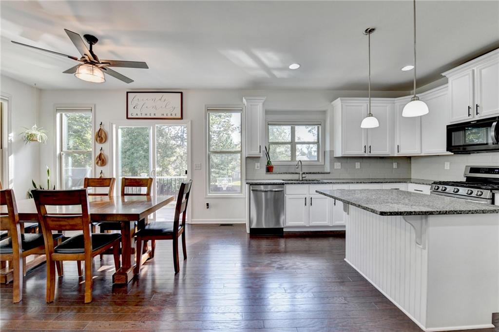 533 Widgeon Way Jefferson, GA 30549 - Photo 30 of 101 a kitchen with stainless steel appliances kitchen island granite countertop a stove a sink a dining table and chairs with wooden floor