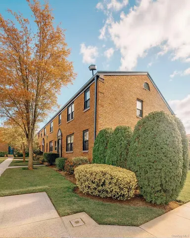a view of a white house next to a yard with big trees