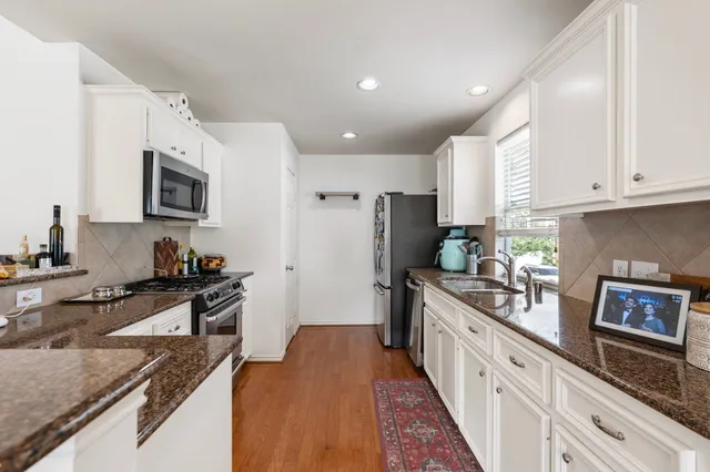 a kitchen with stainless steel appliances granite countertop a stove top oven a sink a refrigerator white cabinets and wooden floor