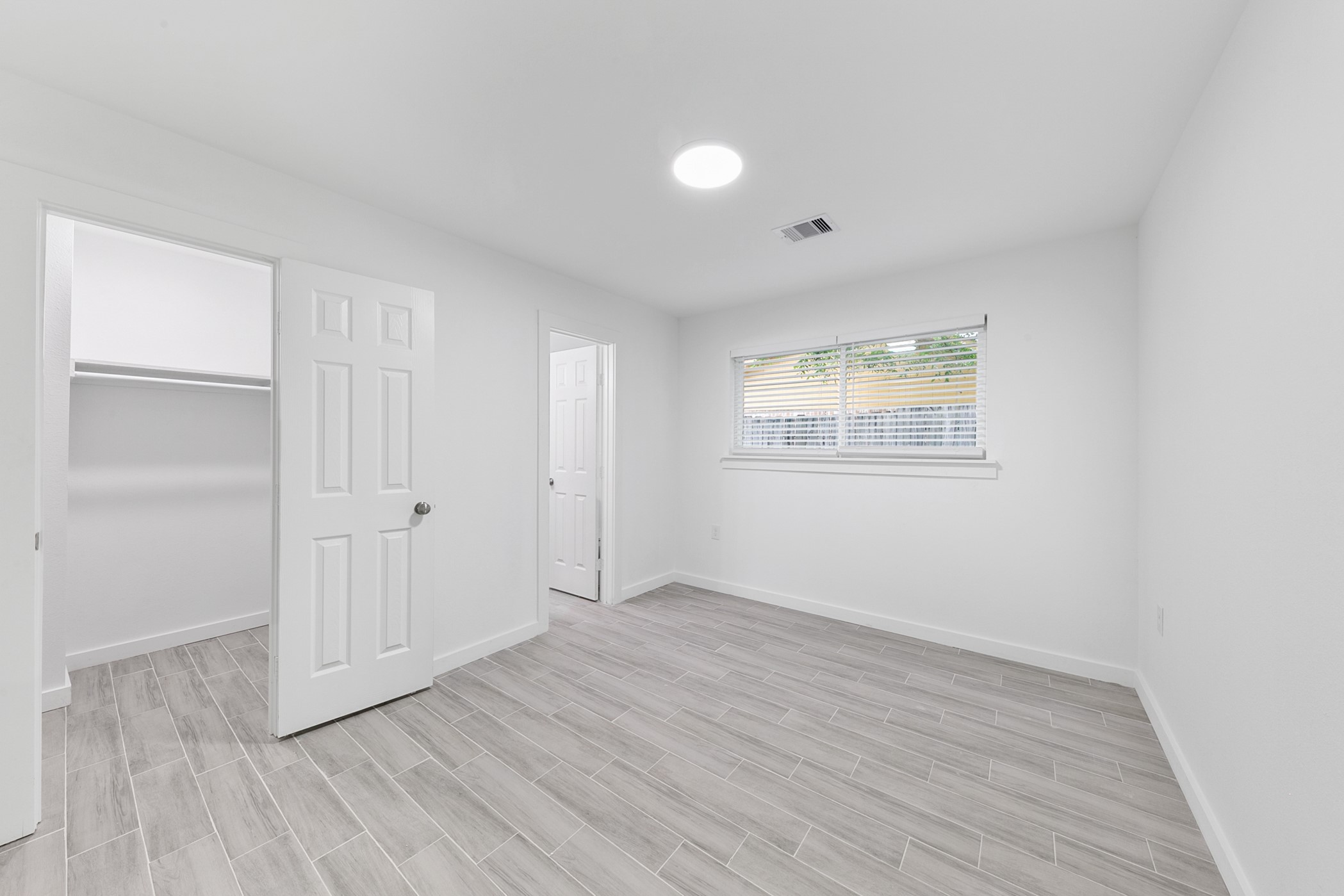 6811 McCullum Road Houston, TX 77489 - Photo 13 of 22 This photo shows a bright, minimalist room with light wood-look tile flooring and white walls. It features a window with blinds, a small closet, and a recessed light, creating a clean and airy atmosphere.