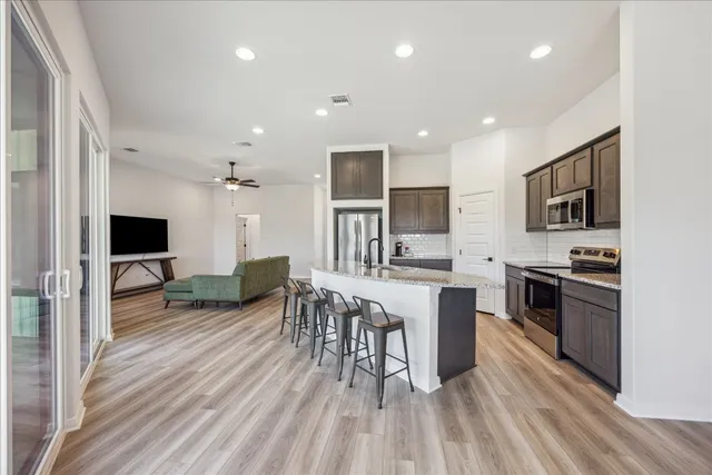 a living room with stainless steel appliances furniture a flat screen tv and kitchen view