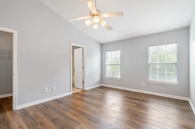 an empty room with wooden floor chandelier fan and windows
