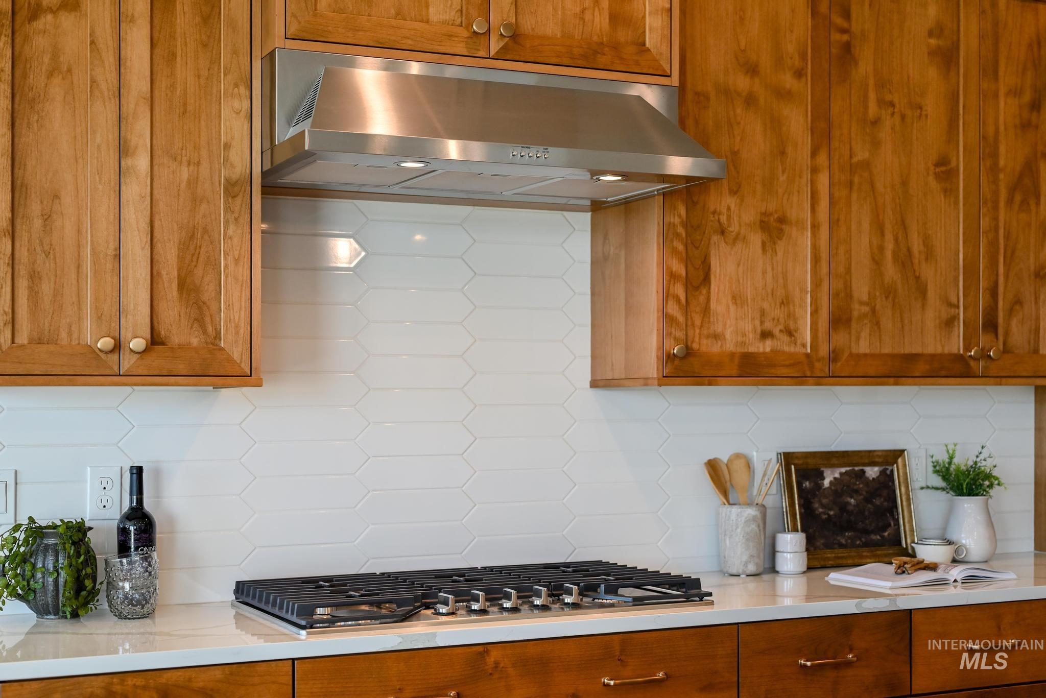 5407 Sparky Avenue Caldwell, ID 83607 - Photo 12 of 41 Kitchen featuring decorative backsplash, brown cabinetry, wall chimney range hood, stainless steel gas stovetop, and light stone counters