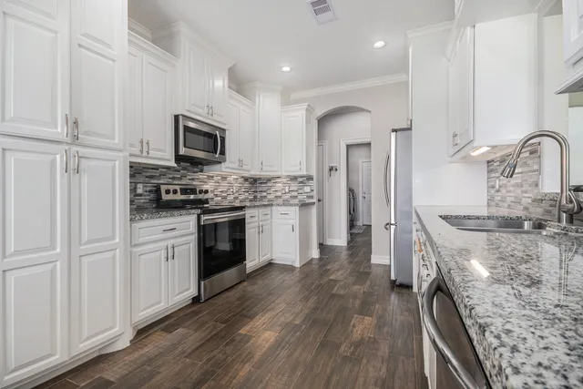 a kitchen with stainless steel appliances granite countertop a stove top oven a sink and white cabinets