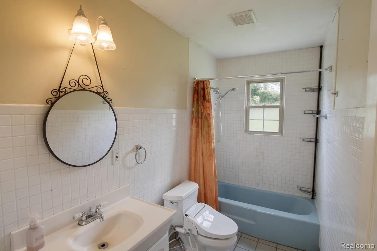 8040 Smith Road Gaines, MI 48436 - Photo 17 of 30 Bathroom featuring a single vanity, a decorative mirror with sconce lighting, and a tiled shower/tub combination