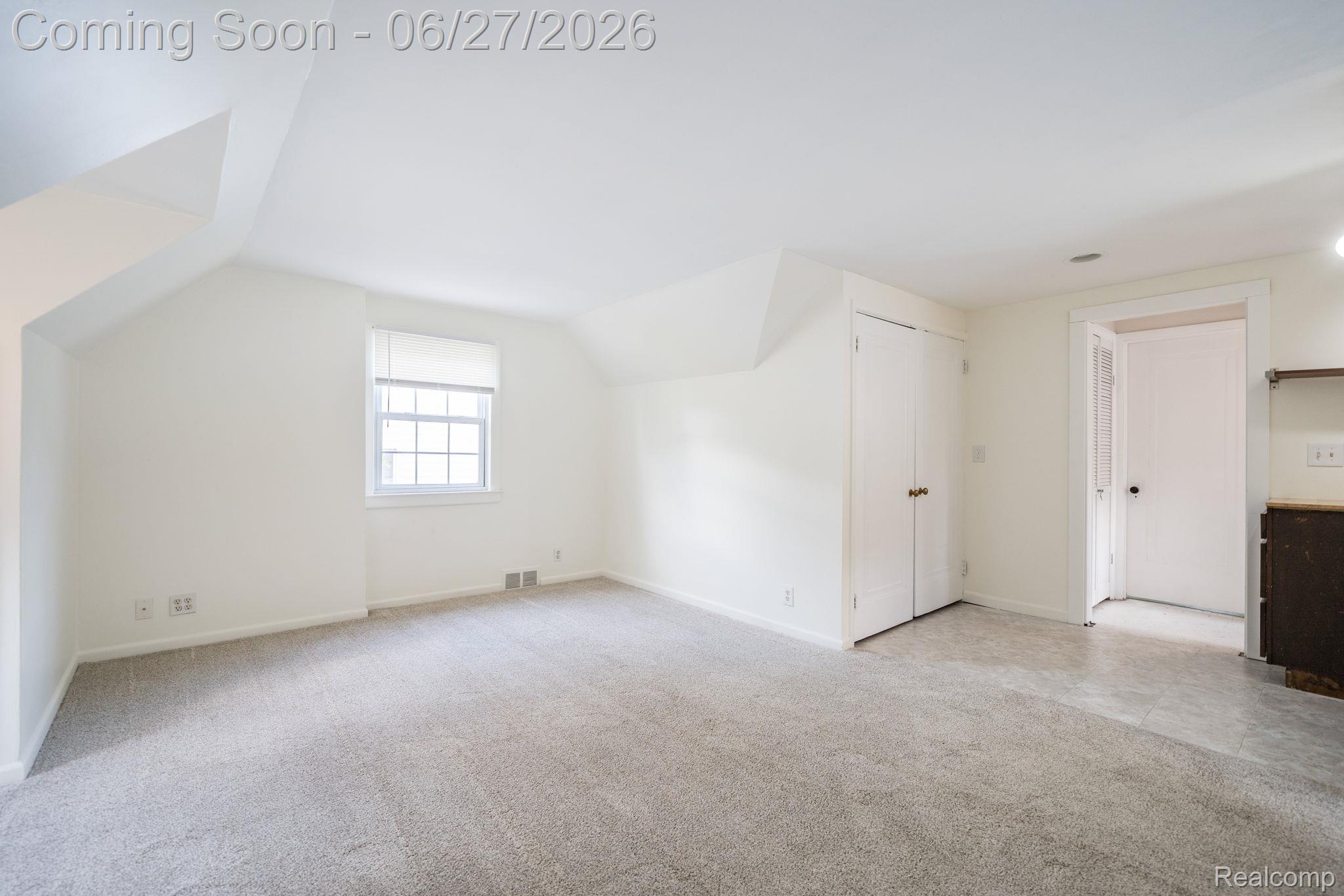 39 Mohawk Road Pontiac, MI 48341 - Photo 21 of 32 Spacious room featuring sloped ceilings, a multi-pane window with a roller shade, light gray carpet, and two white bi-fold closet doors