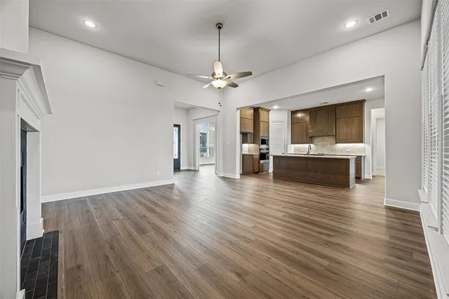an empty room with wooden floor ceiling fan and windows