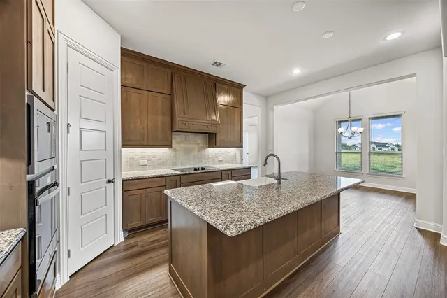 a kitchen with stainless steel appliances granite countertop a sink dishwasher and a refrigerator with wooden floor