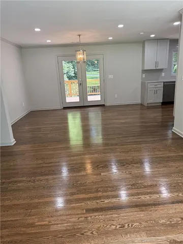 a view of an empty room with kitchen and wooden floor
