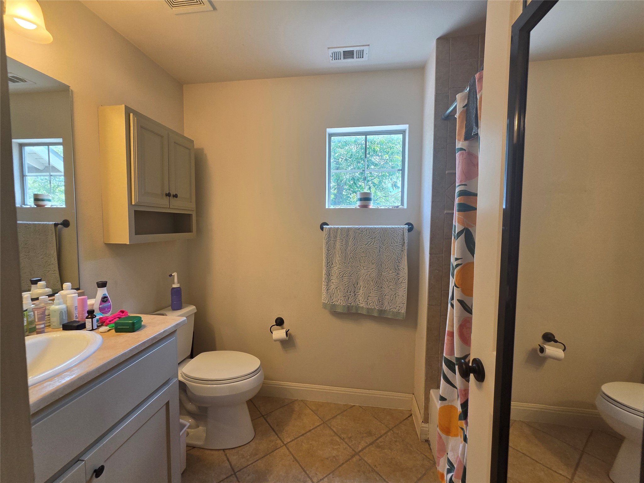 408 West Croslin Street Austin, TX 78752 - Photo 21 of 29 A well-lit lavatory features a single vanity, a toilet, and a tiled shower with a window offering natural light.