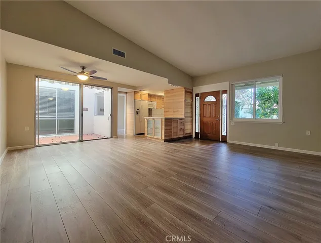 an empty room with wooden floor kitchen view and windows