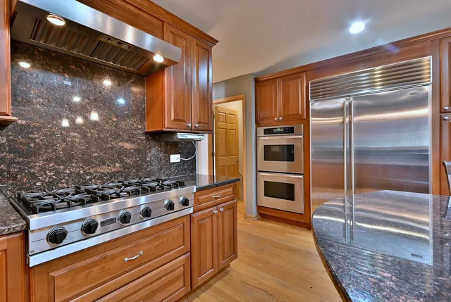 a kitchen with stainless steel appliances granite countertop a stove top oven a sink a dining table and chairs with wooden floor