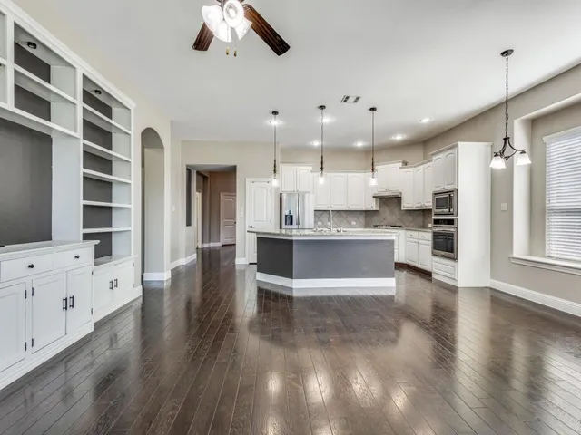 a large kitchen with kitchen island a stove a sink a refrigerator and white cabinets with wooden floor