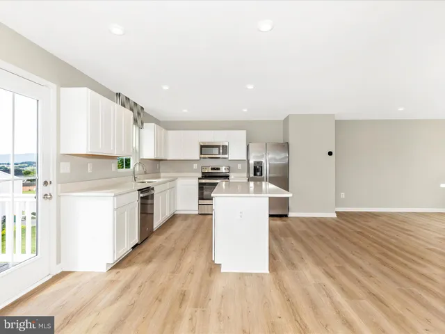 a kitchen with granite countertop a stove top oven a sink a refrigerator and white cabinets with wooden floor