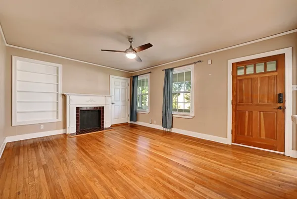 a view of an empty room with wooden floor fireplace and a window