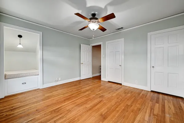 a view of an empty room with wooden floor and a ceiling fan