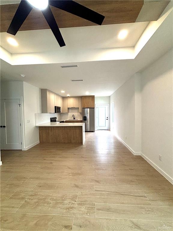 3 Estevan Street Mission, TX 78573 - Photo 13 of 22 Open-concept living space featuring wood-finish flooring, a contemporary kitchen with light cabinetry, stainless steel appliances, and a tray ceiling with recessed lighting
