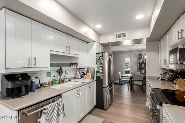 a kitchen with stainless steel appliances granite countertop a refrigerator a sink dishwasher a stove and white cabinets with wooden floor