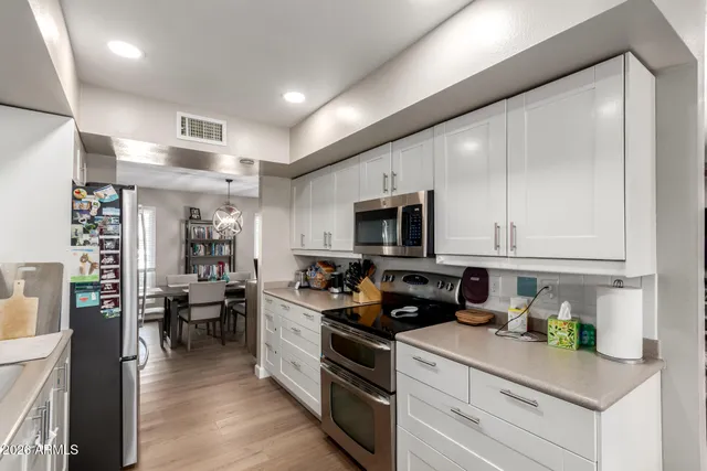 a kitchen with stainless steel appliances granite countertop a refrigerator a stove top oven a sink dishwasher and white cabinets with wooden floor