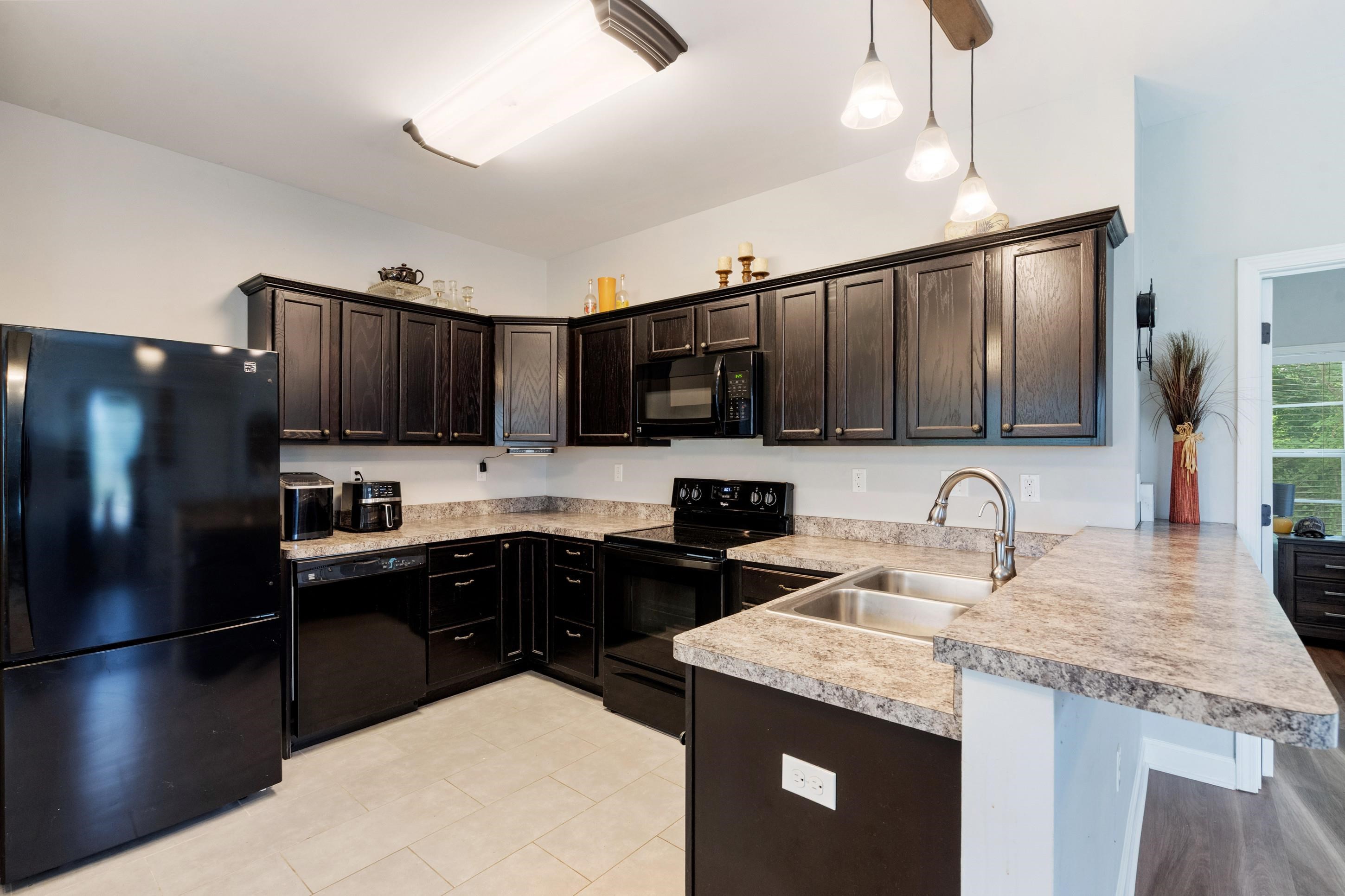 7757 Brunswick Road Millington, TN 38053 - Photo 26 of 40 Kitchen featuring dark wood-finish cabinetry, black appliances, light-toned countertops, a double basin sink with a high-arc faucet, and pendant lighting