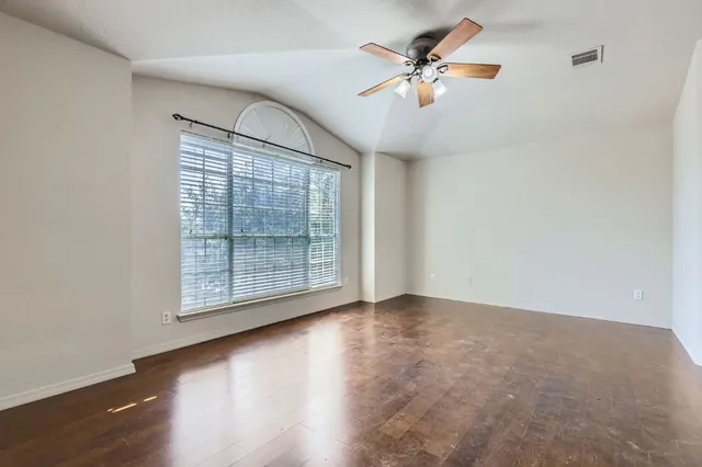 an empty room with wooden floor chandelier fan and windows