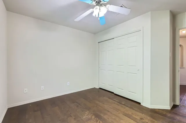 an empty room with a chandelier fan and wooden floor