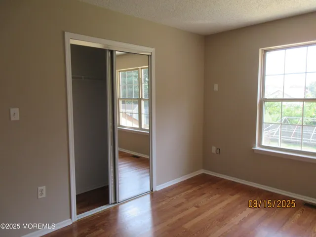 an empty room with wooden floor closet and windows