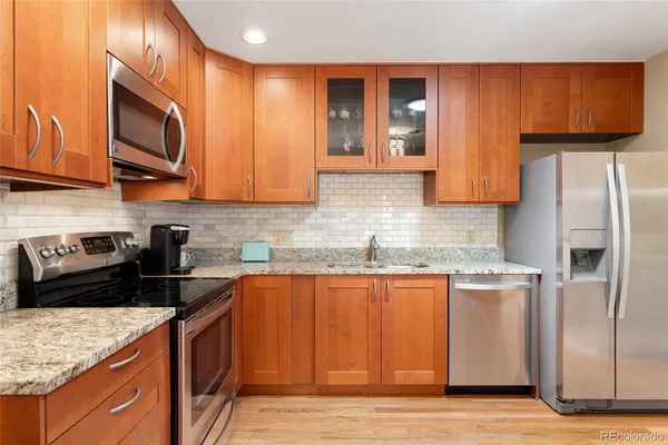 a kitchen with stainless steel appliances granite countertop a stove a sink dishwasher and a refrigerator with wooden cabinets