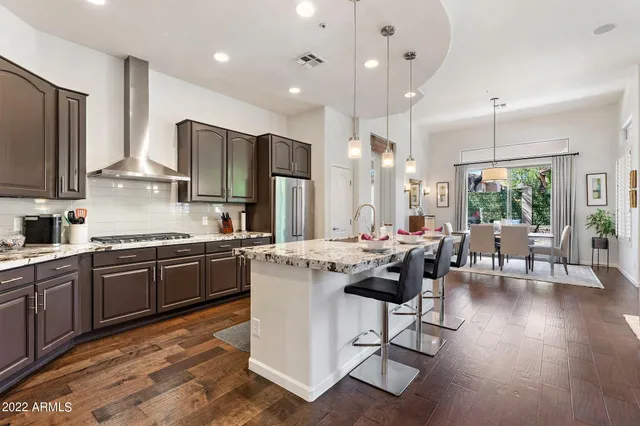 a kitchen with stainless steel appliances granite countertop a stove a sink a refrigerator a dining table and chairs