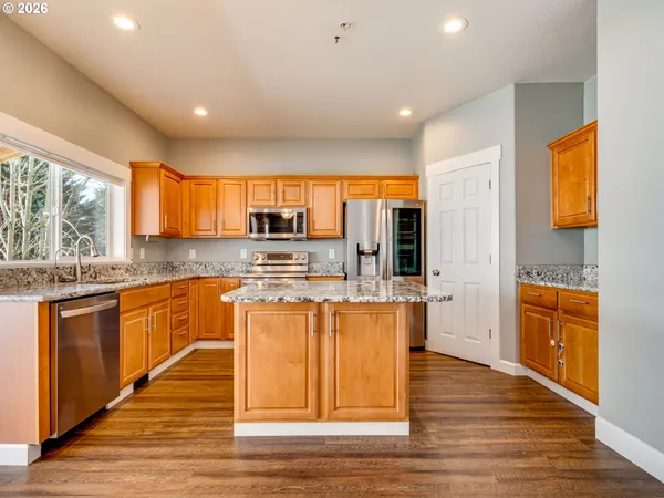a large kitchen with stainless steel appliances granite countertop a stove a sink dishwasher and a large refrigerator with wooden floor