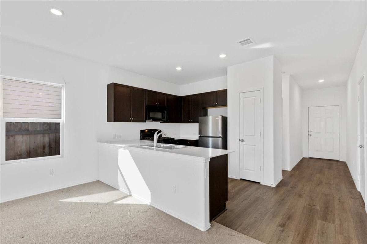14320 Tordillo Drive Elgin, TX 78621 - Photo 5 of 19 Kitchen featuring dark wood finish cabinetry, a peninsula, freestanding refrigerator, black microwave, and gas range