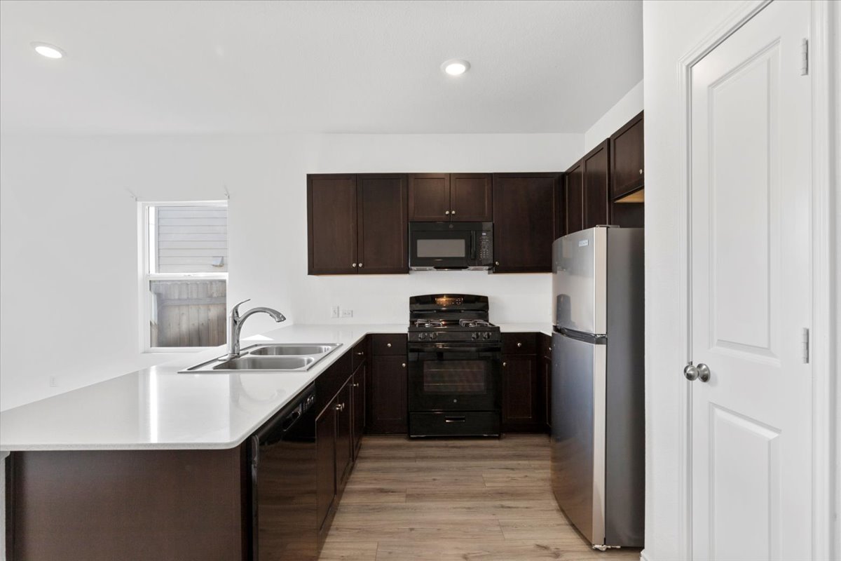 14320 Tordillo Drive Elgin, TX 78621 - Photo 6 of 19 Kitchen with dark wood finish cabinets, black appliances, a peninsula, light wood-style floors, and recessed lighting