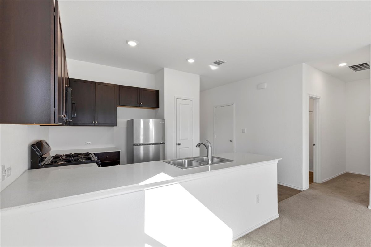 14320 Tordillo Drive Elgin, TX 78621 - Photo 8 of 19 Kitchen featuring a peninsula, stainless steel appliances, light countertops, dark wood finish cabinets, and light carpet