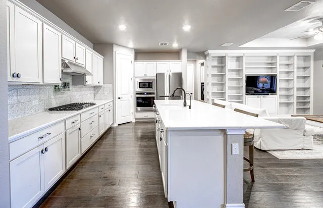 a kitchen with stainless steel appliances a stove top oven a sink a refrigerator white cabinets and wooden floor
