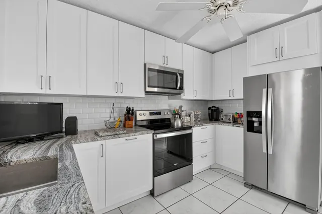 a kitchen with stainless steel appliances granite countertop a refrigerator stove a sink and white cabinets