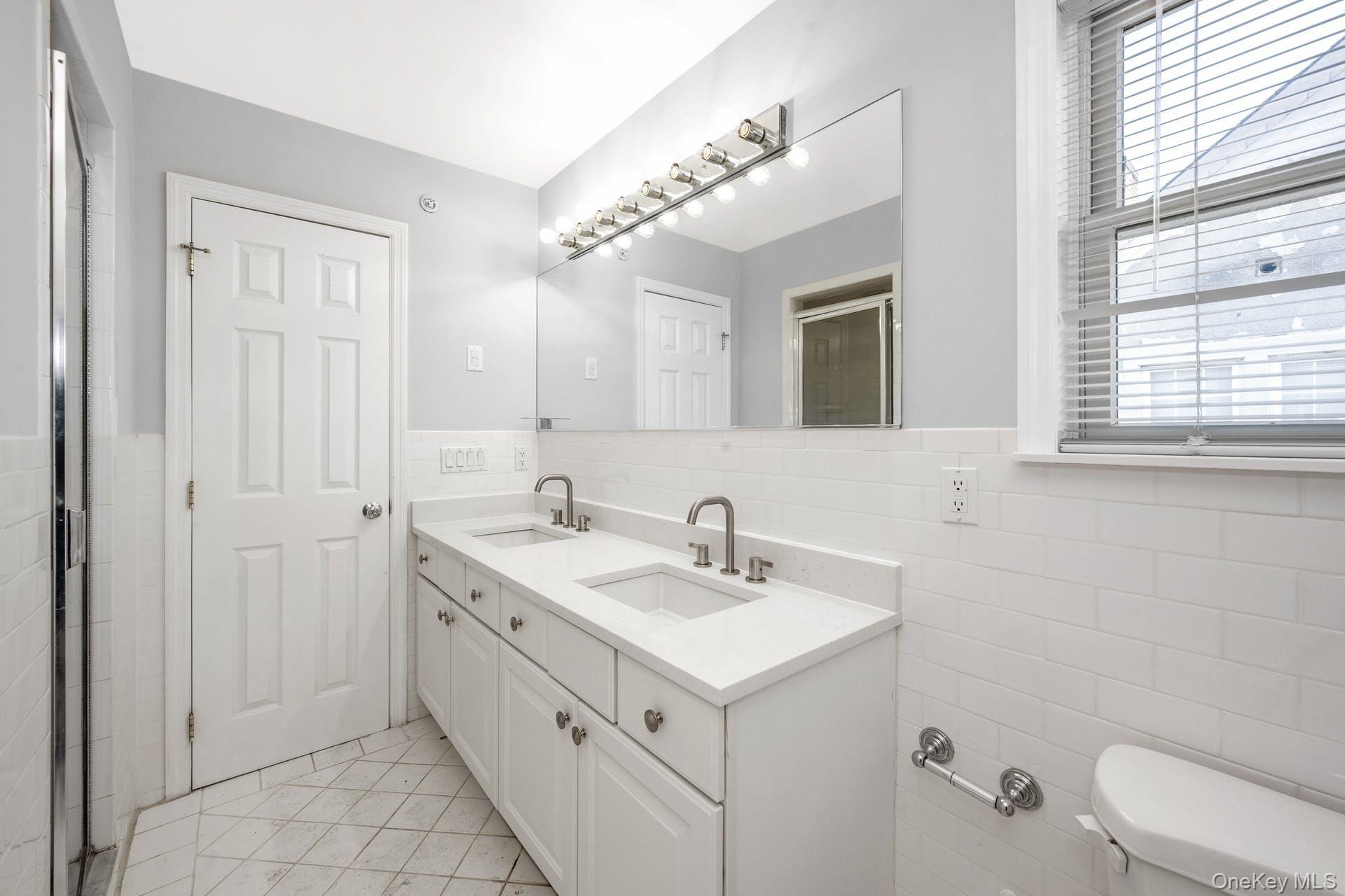 69 Ellsworth Avenue Harrison, NY 10528 - Photo 17 of 28 Bathroom with tile walls, double vanity, a wainscoted wall, and tile patterned flooring