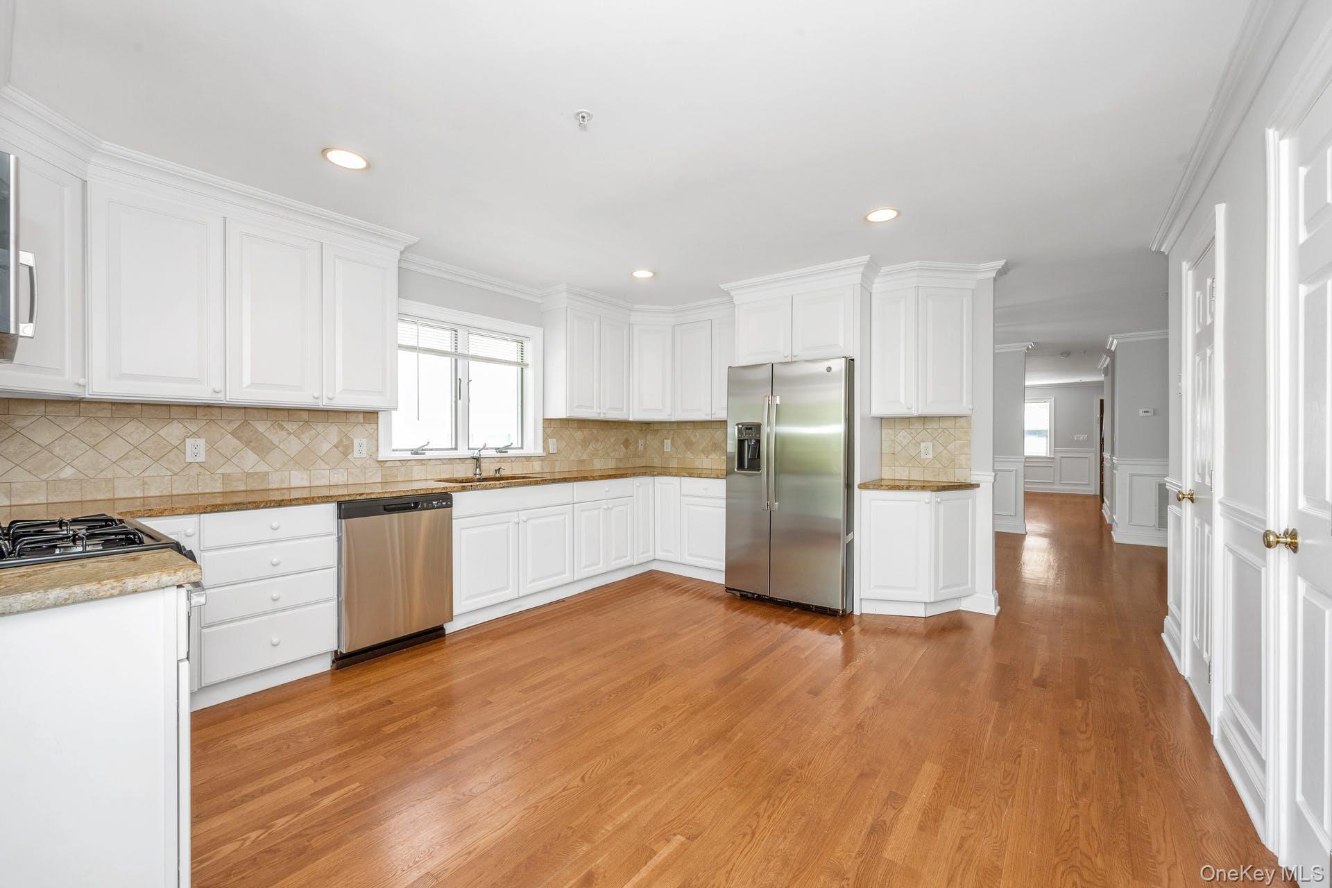 69 Ellsworth Avenue Harrison, NY 10528 - Photo 7 of 28 Kitchen featuring stainless steel appliances, light wood-style flooring, white cabinets, backsplash, and crown molding