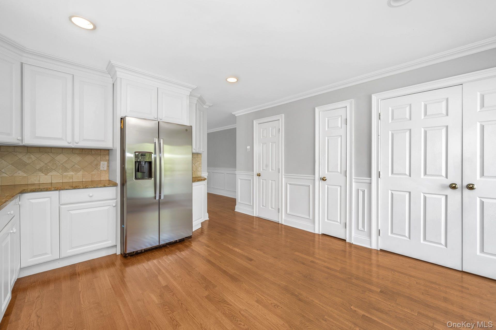 69 Ellsworth Avenue Harrison, NY 10528 - Photo 9 of 28 Kitchen featuring stainless steel fridge with ice dispenser, white cabinets, light wood finished floors, ornamental molding, and recessed lighting