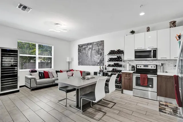 a living room with stainless steel appliances furniture a flat screen tv and a kitchen view