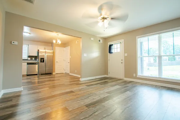 a view of an empty room with wooden floor and a kitchen