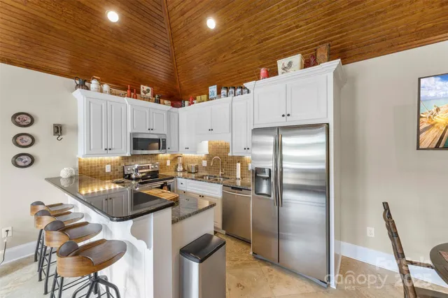 a kitchen with stainless steel appliances granite countertop a refrigerator a stove a sink dishwasher and white cabinets with wooden floor