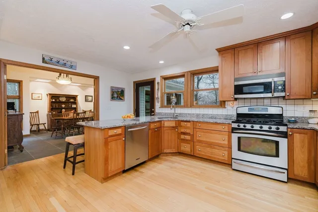 a kitchen with stainless steel appliances granite countertop a stove top oven a sink dishwasher a dining table and chairs with wooden floor