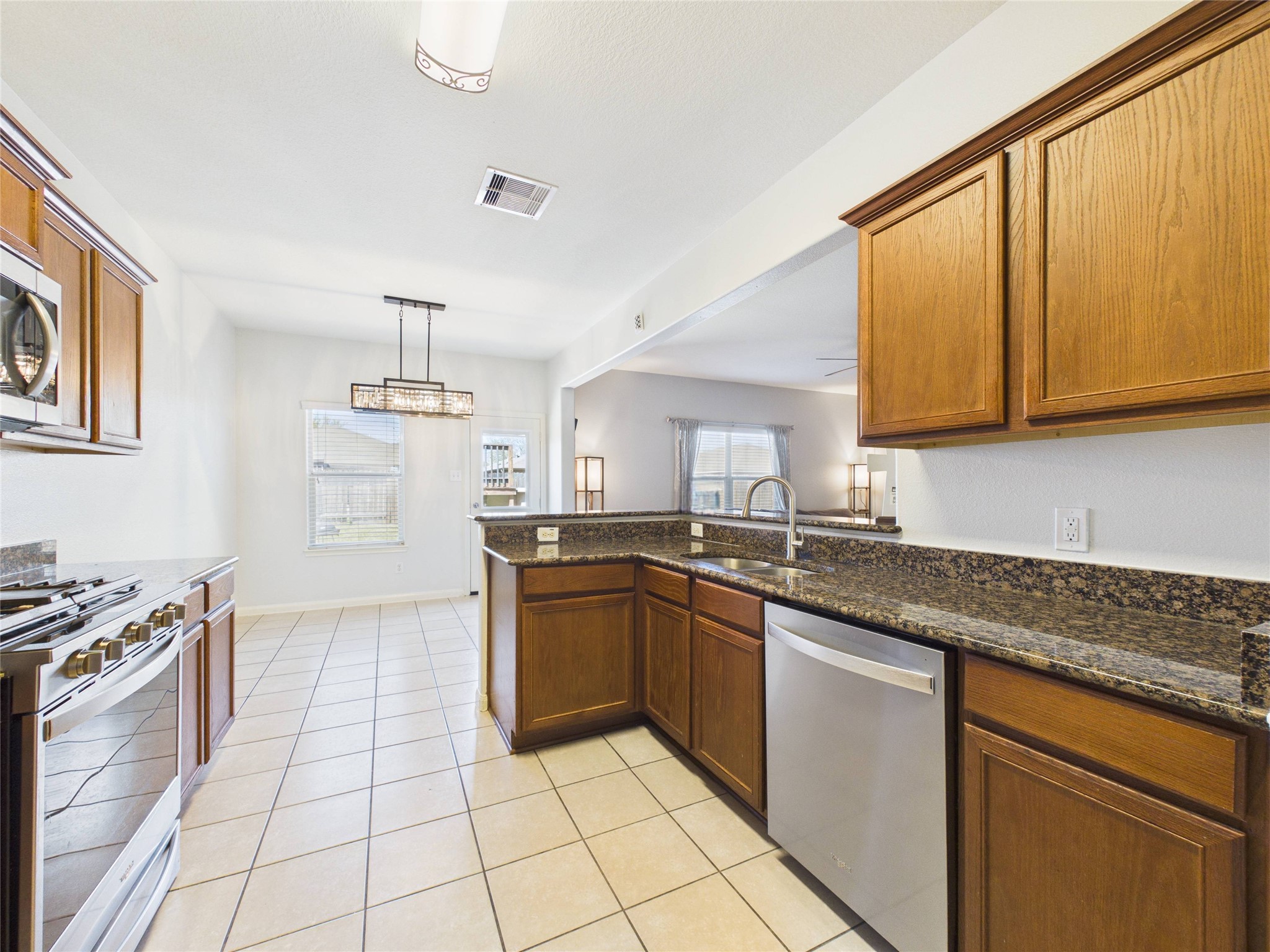 911 Marigold Road Baytown, TX 77521 - Photo 15 of 33 Spacious kitchen with sleek granite countertops, stainless steel appliances, and warm wood cabinetry, opening to a bright dining area.